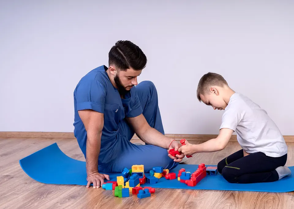 Terapeuta ocupacional juega con bloques de construcción con un niño sobre una esterilla